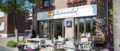 A hotel restaurant with outdoor seating, flower planters, and a signboard.