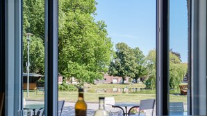 A table with a bottle, glasses, and a menu, overlooking a park with a pond and trees. - Hotel Schwanenhof (Erkelenz)
