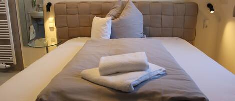 Una cama bien hecha con cabecera marrón, almohadas blancas y una toalla doblada.