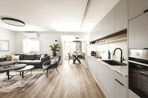 Ein modernes Wohnzimmer mit einer Couch, einem Couchtisch und Sesseln, ein Essbereich mit Tisch und Stühlen sowie eine Küche mit Schränken und Geräten.