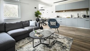 Een moderne woonkamer met een grijze bank, een salontafel en een eethoek met een plant.