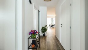 Een hal met een houten vloer, witte muren, een zwart metalen schap met een bloevas en een potplant.
