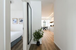 A hallway with a bed, a potted plant, and a dining area with a table and chairs.
