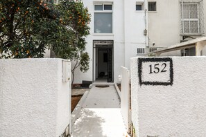 A narrow pathway leading to a building entrance with a white exterior and a number '152' sign. - Relax in a Rural Retreat 2BR Apt wGarden (Ramat Hasharon)