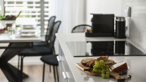 Een moderne keuken met een eethoek, met een wit aanrecht waarop kaas en druiven zijn uitgestald, een koffieapparaat en een eettafel met stoelen.