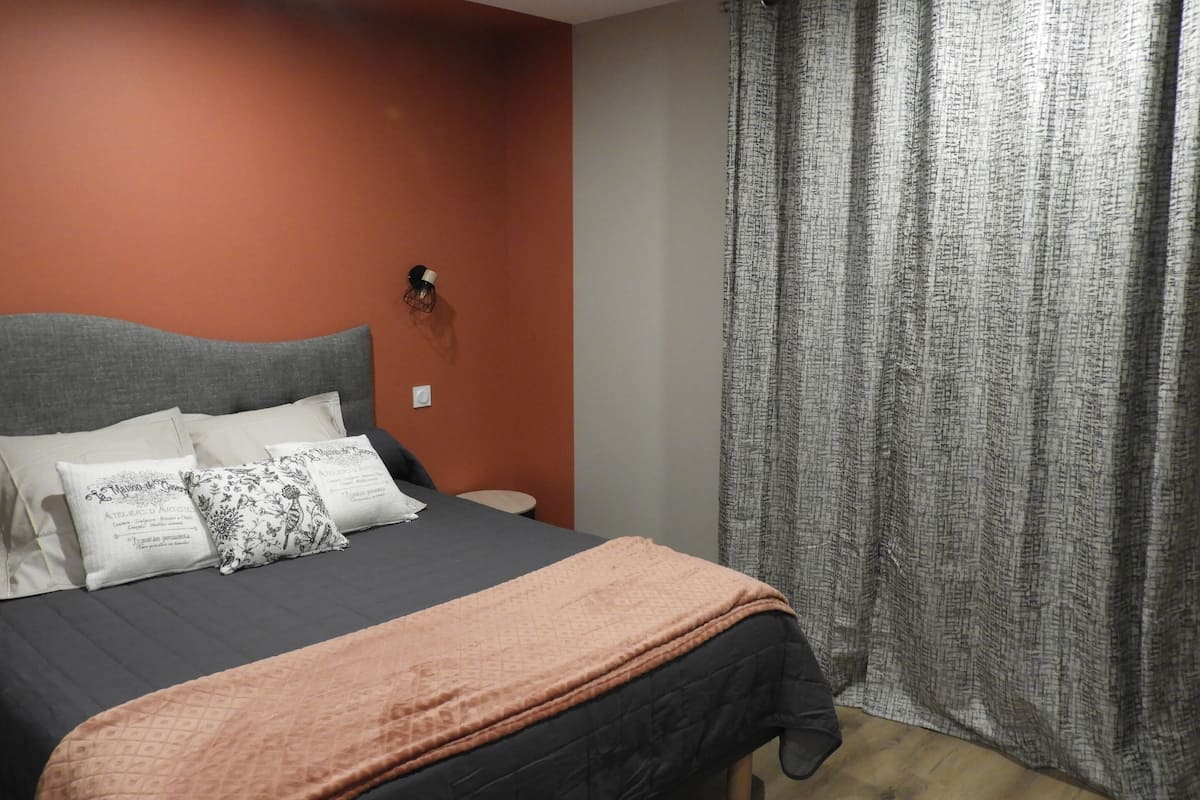 A bedroom with a bed, pillows, a nightstand, and a curtain.