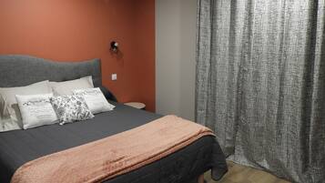 Un dormitorio con cama, almohadas, una mesita de noche y una cortina.