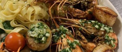 A plate of food including grilled shrimp, scallops, pasta, and a salad with a cherry tomato and shredded carrots.