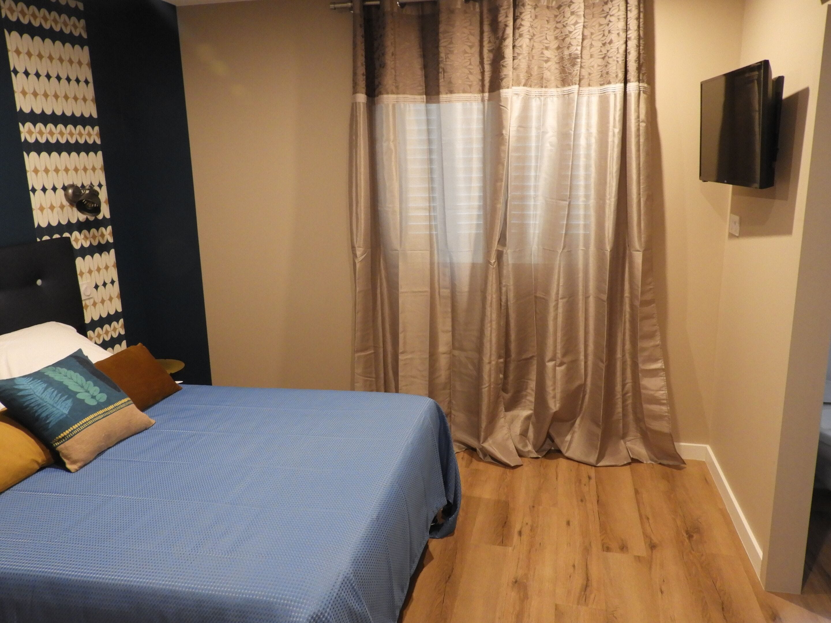 A bedroom with a bed, a TV mounted on the wall, and a curtain.