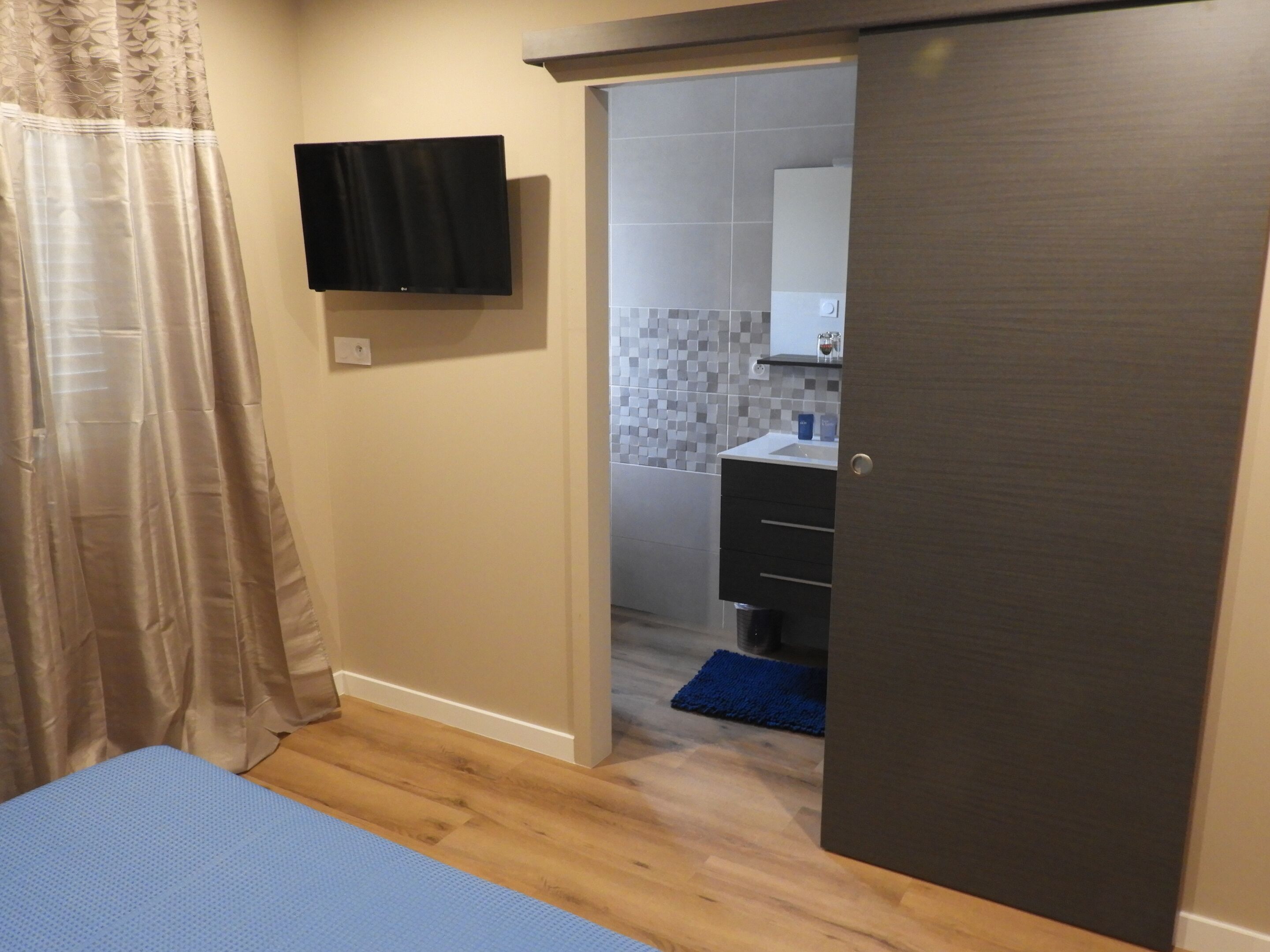 A bedroom with a bed, a television mounted on the wall, and a bathroom visible through an open door.