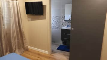 A bedroom with a bed, a television mounted on the wall, and a bathroom visible through an open door.