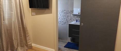 A bedroom with a bed, a television mounted on the wall, and a bathroom visible through an open door.