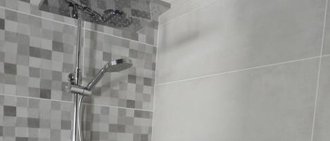 A shower with a chrome finish, a tiled wall with a checkered pattern, and a plain tiled wall.