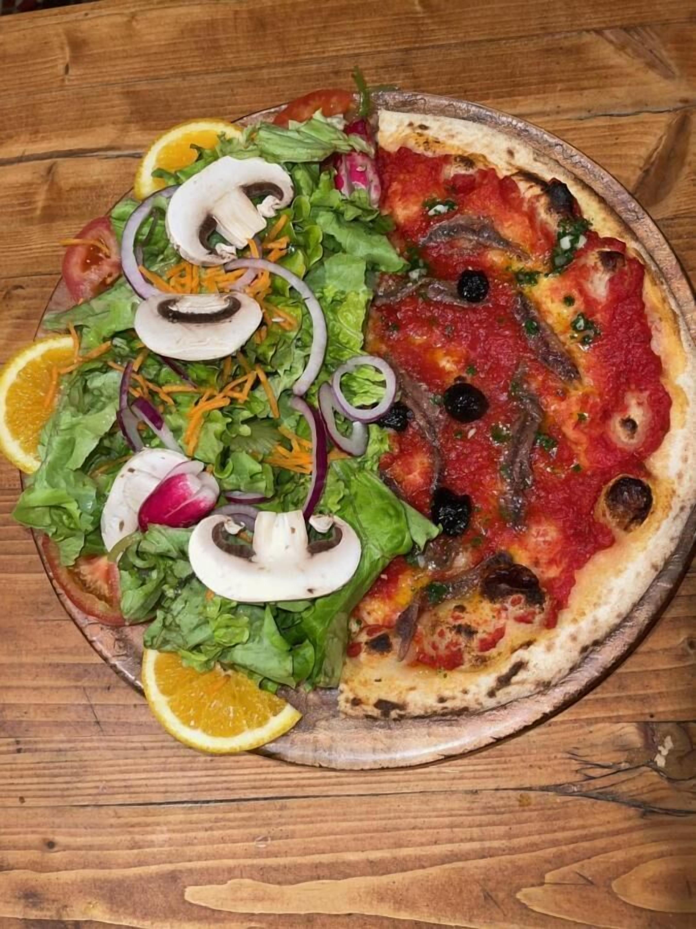 Eine Pizza mit Belag und ein Salat auf einem Holztisch.