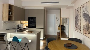 A modern kitchen with built-in appliances, a dining area with a wooden table and bar stools, and a staircase leading to another level. - APARTAMENTO  NUEVO, LUJOSO, CENTRO DE BILBAO. (Bilbo)
