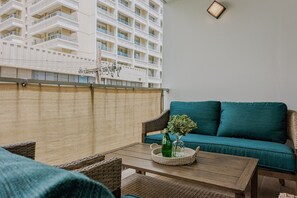 A balcony with a wicker sofa, a wooden table, and a decorative plant.