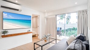 Ein modernes Wohnzimmer mit großem Flachbildfernseher, einer Couch, einem Couchtisch und einem Balkon mit Vorhängen.