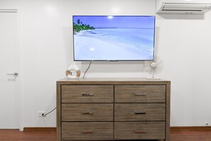 A room with a TV on a wooden cabinet, a wall-mounted air conditioner, and a power outlet.