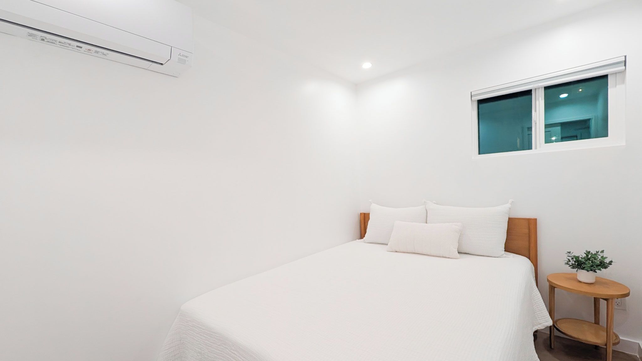 Un dormitorio minimalista con una cama, una mesita de noche con una planta y una ventana.