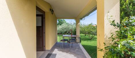 Un patio techado al aire libre con mesa y sillas, una puerta y vistas a un jardín.