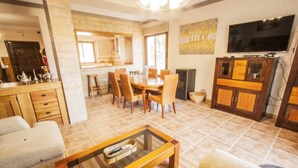 A spacious living room with a dining area, kitchen, and a TV mounted on the wall.