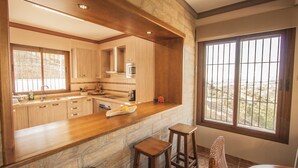 A kitchen with wooden cabinets, a stone countertop, and a view through large windows.
