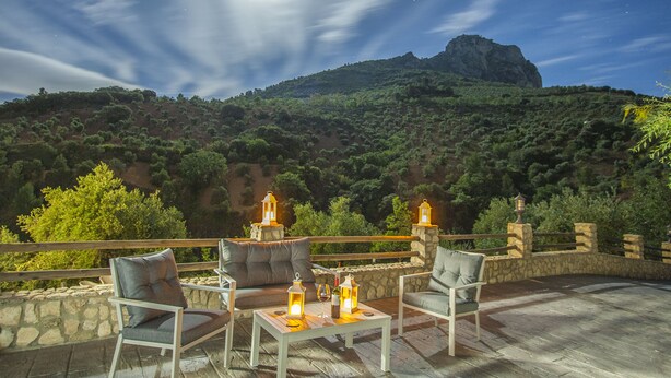 A terrace with outdoor seating and lanterns, overlooking a mountainous landscape.