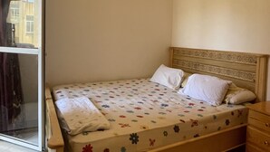 Un lit simple avec une couvre-lit à motifs floraux, une tête de lit en bois et une table de chevet en bois dotée de tiroirs.