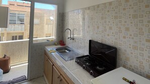 Une cuisine équipée d’une cuisinière à gaz, d’un évier et d’une fenêtre donnant sur un immeuble.