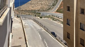 Une route côtière offrant une vue sur la mer et une colline rocheuse à l’horizon.
