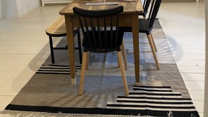 A dining area with a wooden table, black chairs, a patterned rug, and a white cabinet with a mirror.