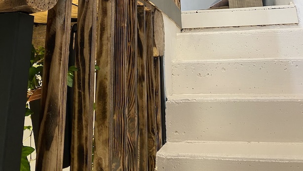 A wooden staircase with a rustic design, leading to a white-walled area with a potted plant.