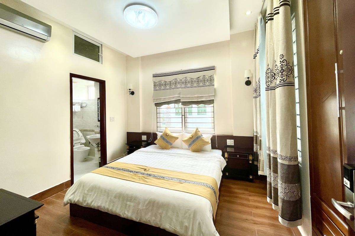 Una habitación de hotel con cama, mesitas de noche, ventana con cortinas, puerta y aire acondicionado.