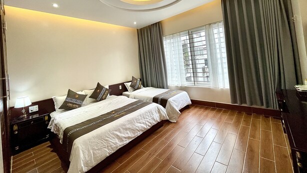 A hotel room with two beds, a large window with curtains, a wooden floor, and a modern ceiling design. - LIBRA HOTEL (Mong Cai)