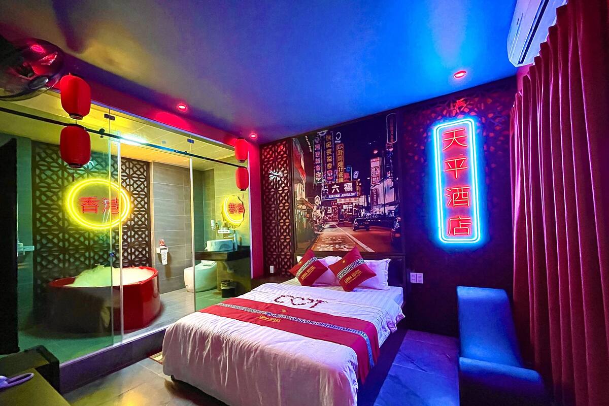Una habitación de hotel moderna con una cama, zona de estar, separador de vidrio y un mural con vista a la ciudad.