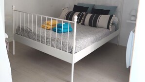 A single-bed room with a white metal frame, grey patterned bedding, and a white ceiling light. - Les Insolites de Champeix 3 (Champeix)