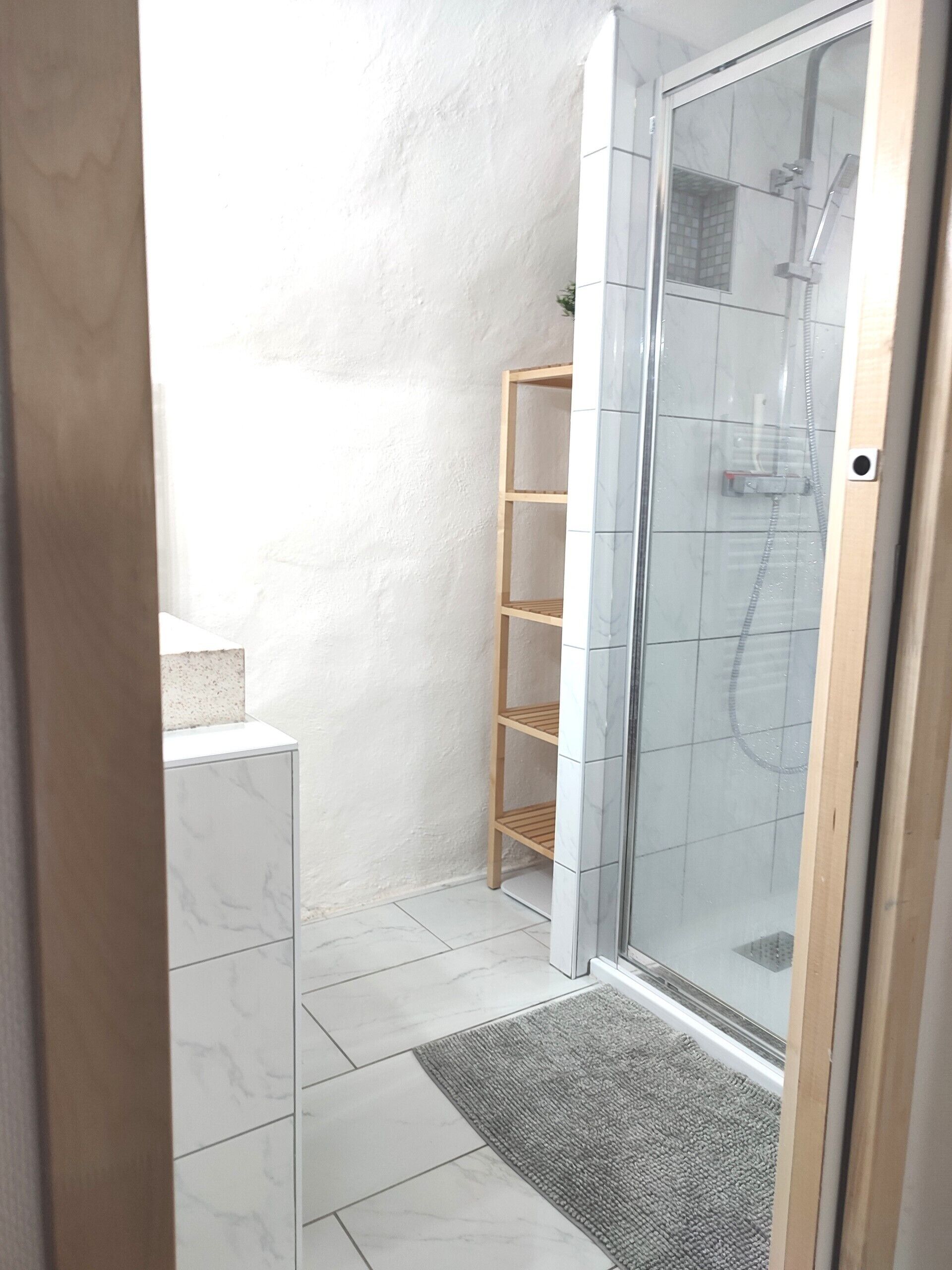 Een moderne badkamer met een douche met glazen wand, een houten plankunit en marmeren vloeren.