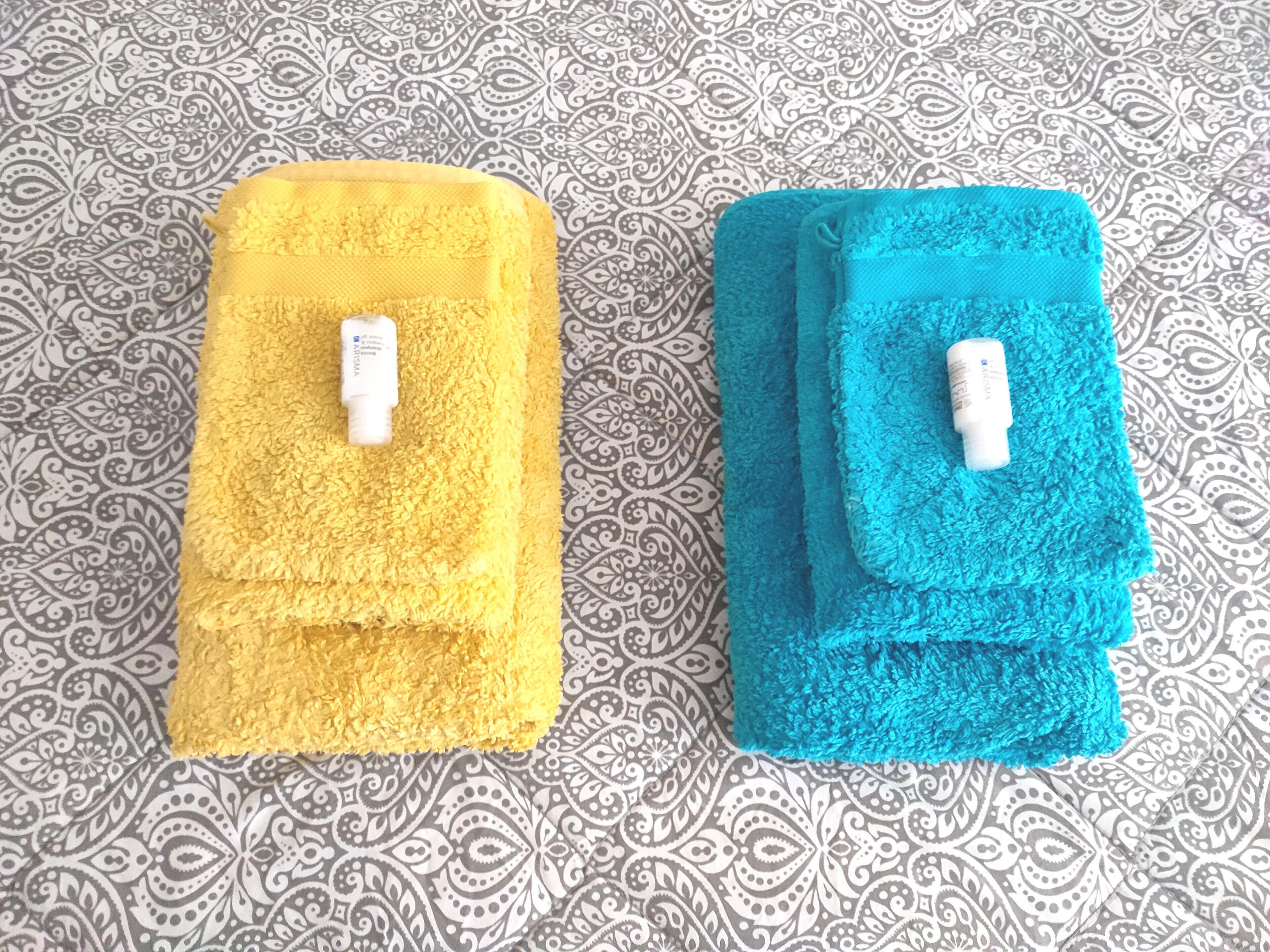 Twee gevouwen handdoeken, een geel en een blauw, met een desinfecterende handgel erbovenop.