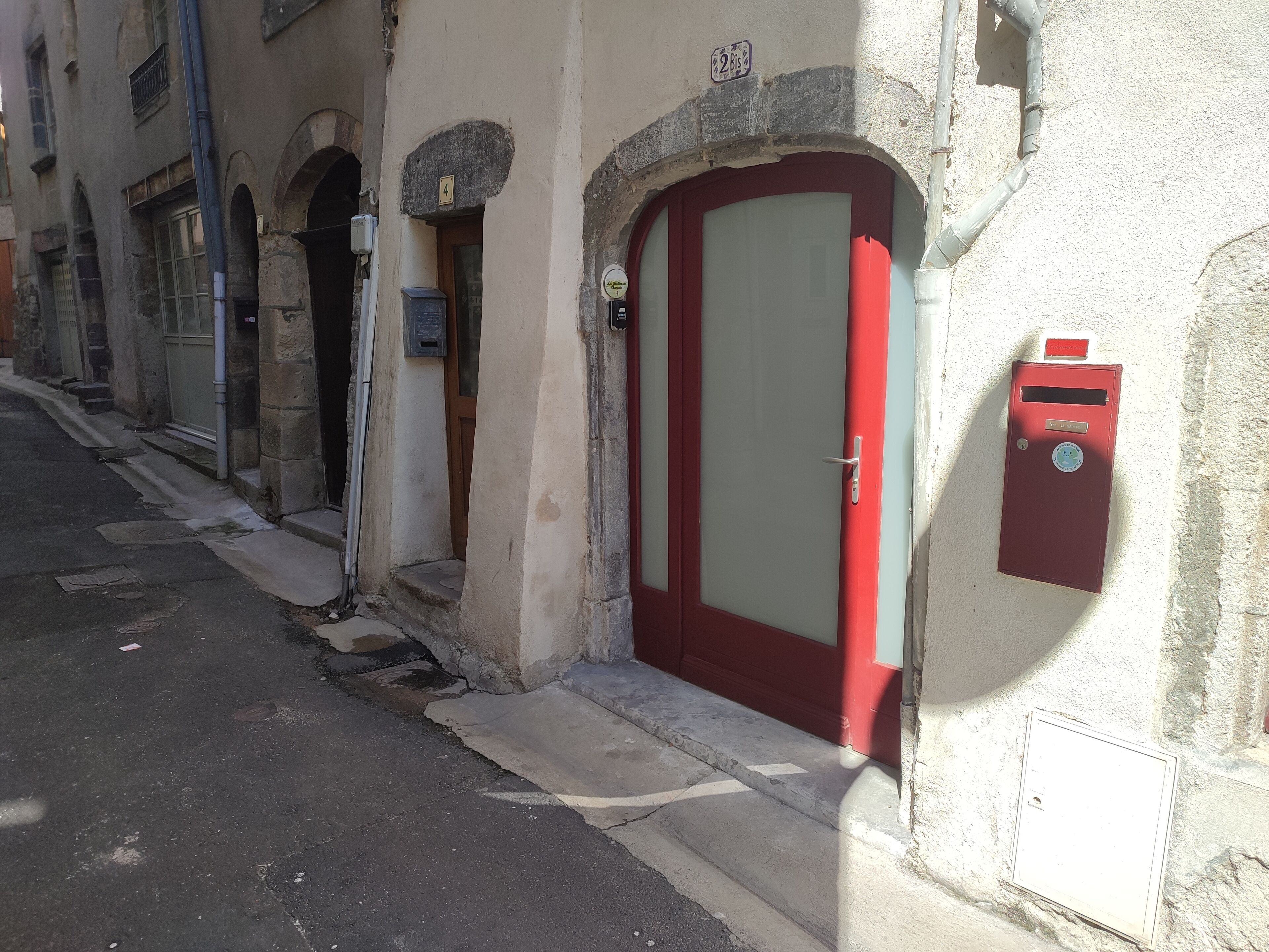Une rue étroite avec une porte rouge et une boîte aux lettres sur le côté droit.