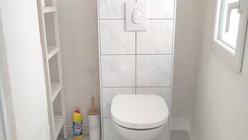 Une petite salle de bain propre, équipée de toilettes, d’une étagère et d’une fenêtre.