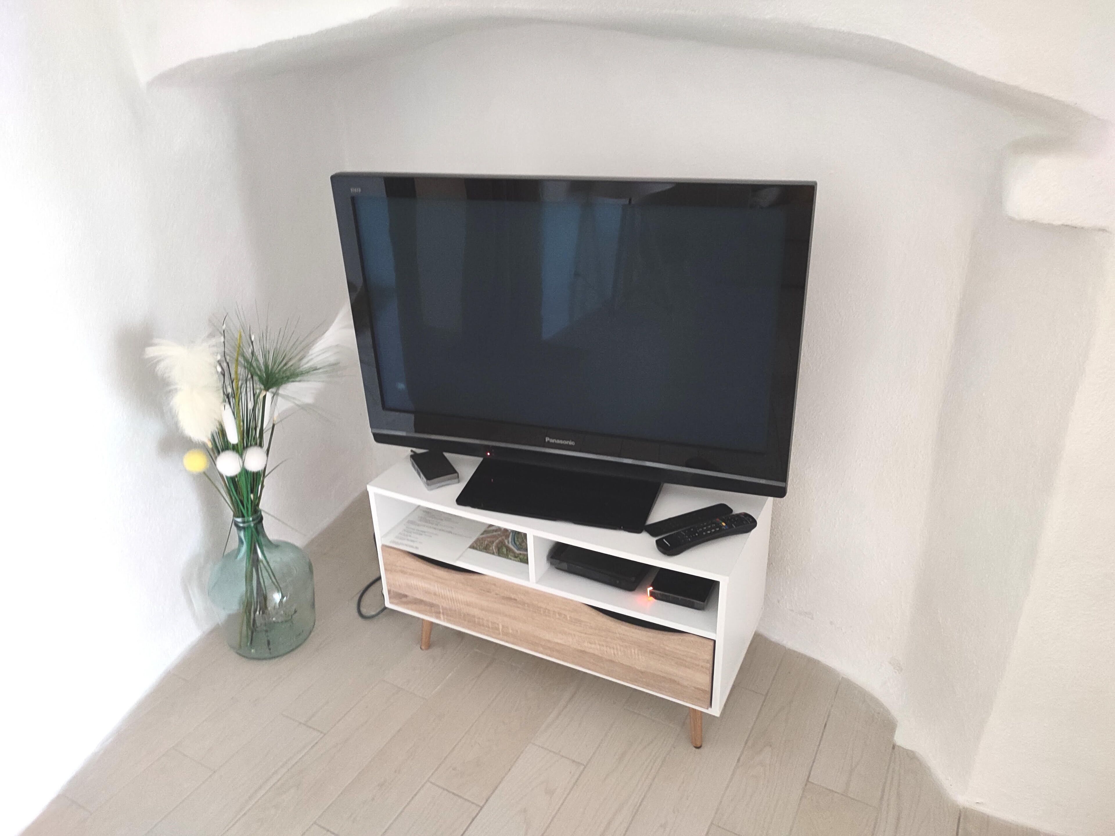 A flat-screen TV on a white entertainment unit with a remote control and a smartphone.