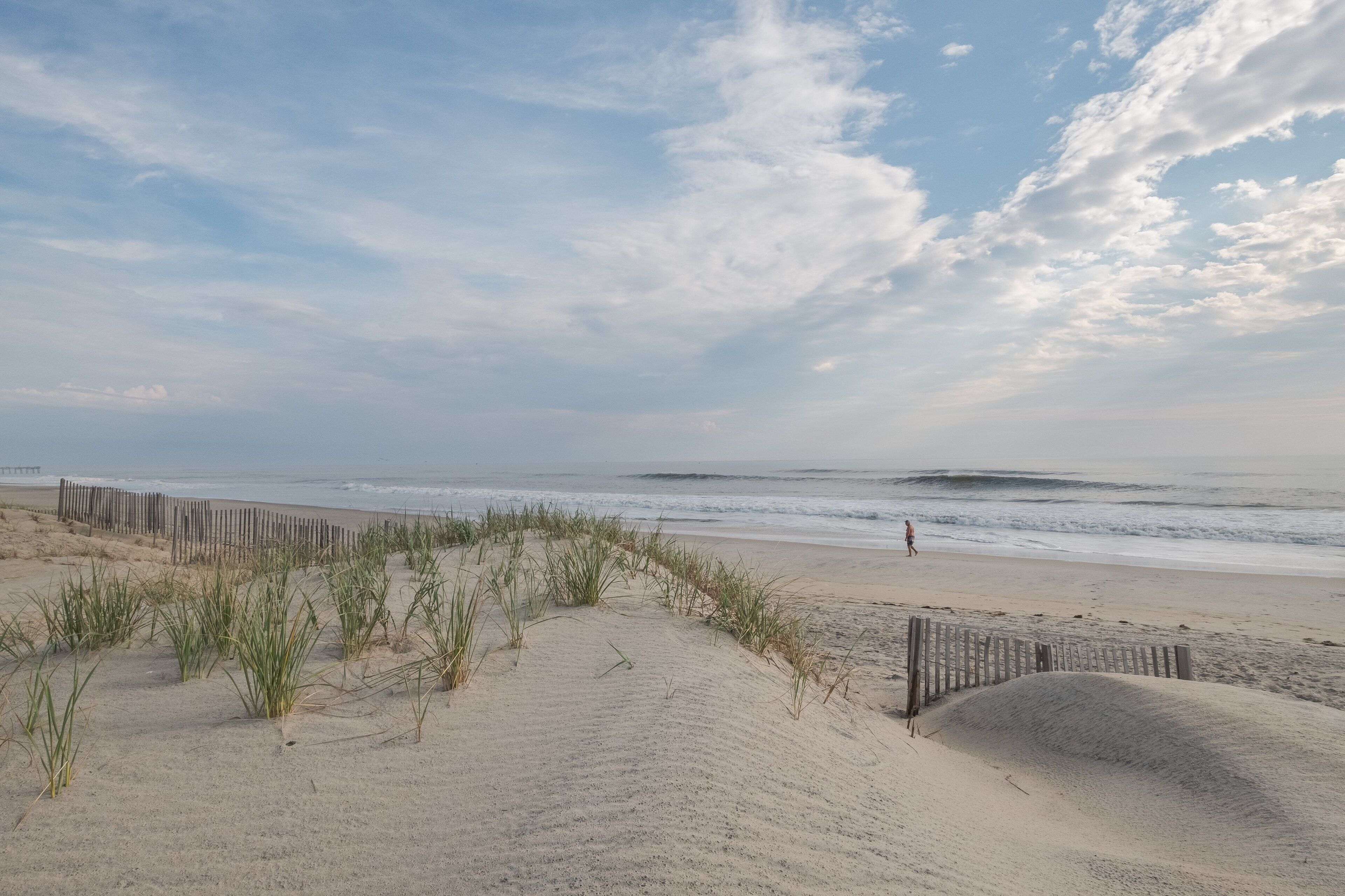 Une plage de sable bordée d’une clôture en bois et de dunes herbeuses.
