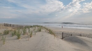 A sandy beach with a wooden fence and grassy dunes. - 5852 - Lega Sea - Oceanfront Cottage | Pool, Views & Hot Tub (Nags Head)