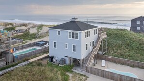 A two-story beach house with a pool, a deck, and a staircase leading to the second floor. - 5852 - Lega Sea - Oceanfront Cottage | Pool, Views & Hot Tub (Nags Head)