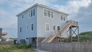 A two-story house with a wooden deck and a staircase leading to the second floor. - 5852 - Lega Sea - Oceanfront Cottage | Pool, Views & Hot Tub (Nags Head)