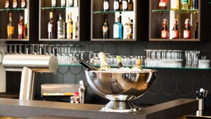 A bar area with a metal bowl containing bottles and glasses, a coffee machine, and shelves with various bottles in the background. - Hotel am Markt (Wipperfuerth)