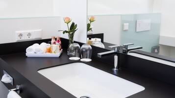 A modern bathroom with a black countertop, a white sink, and a large mirror. There are toiletries on the counter and a vase with a single rose.