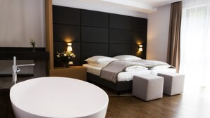 A modern hotel room with a large white bathtub, a dark headboard, and a wooden floor. - Hotel am Markt (Wipperfuerth)