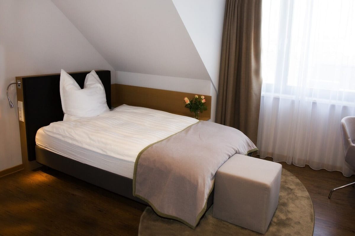 A bedroom with a bed, a nightstand, a chair, and a window with curtains.