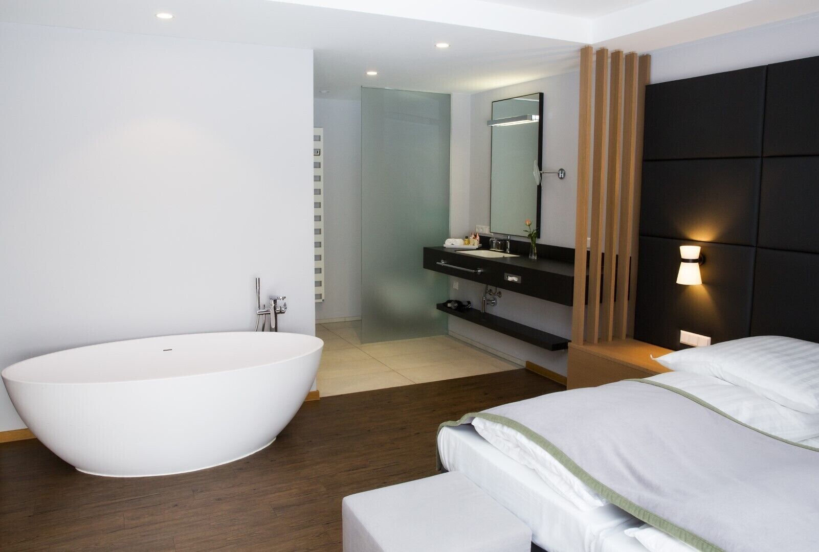 Casa de banho moderna com uma banheira independente, toucador com espelho e cama com roupa de cama branca.